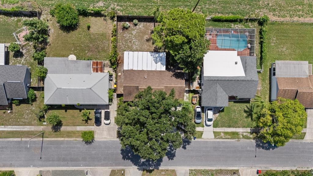 An aerial view shows three residential houses with driveways, trees, and a backyard swimming pool — 1310 MANDARIN DRIVE, HOLIDAY, FL