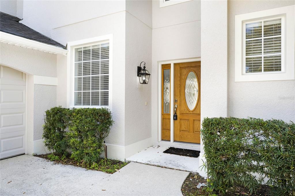The exterior of a house features a wooden front door, a window, and green hedges — 5270 RISHLEY RUN WAY, MOUNT DORA, FL