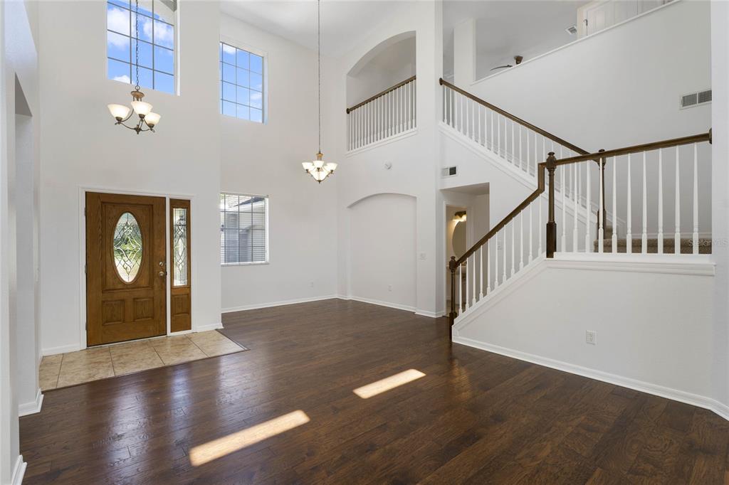 A high-ceilinged foyer features dark wood flooring, a wooden front door, and a staircase — 5270 RISHLEY RUN WAY, MOUNT DORA, FL