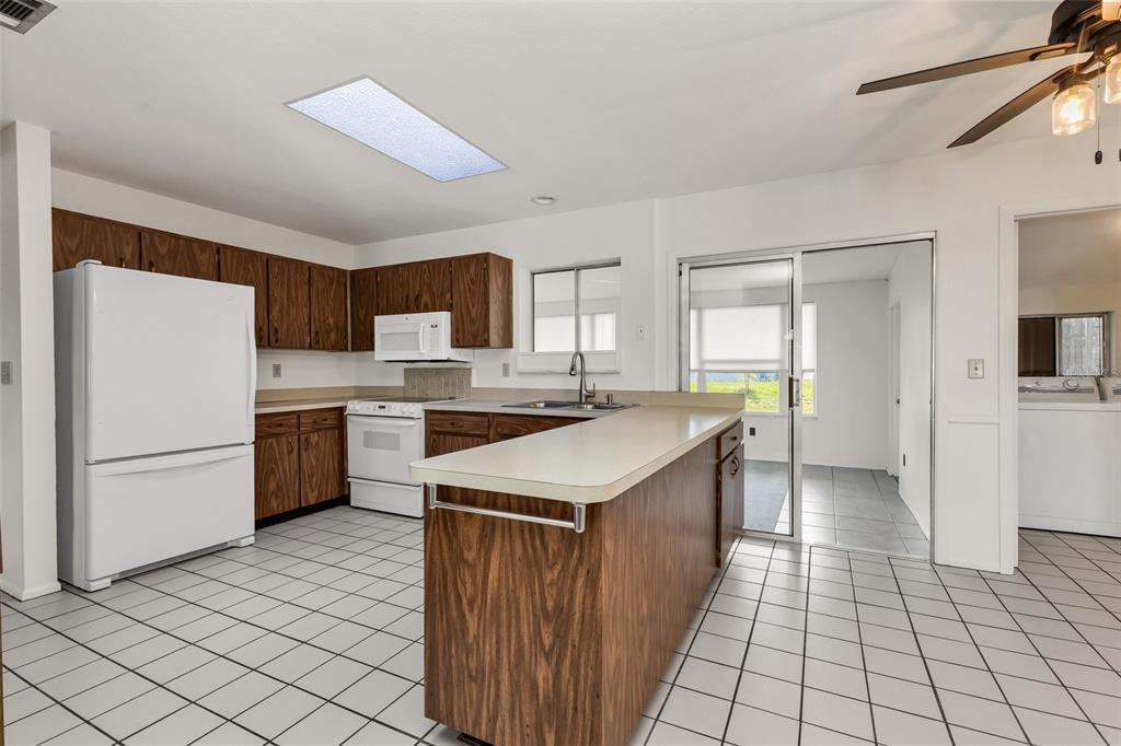 A kitchen features wood cabinets, white appliances, a peninsula, and white tile flooring — 4100 GROBE STREET, NORTH PORT, FL