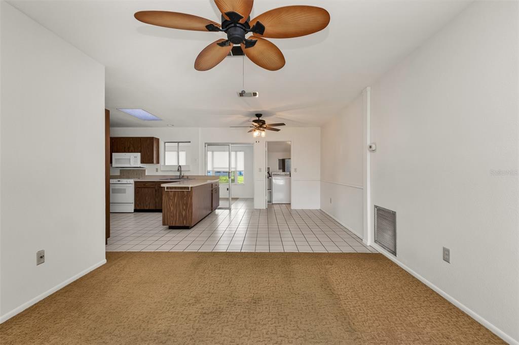 A living room with tan carpet transitions to a tiled kitchen area with wood cabinets — 4100 GROBE STREET, NORTH PORT, FL