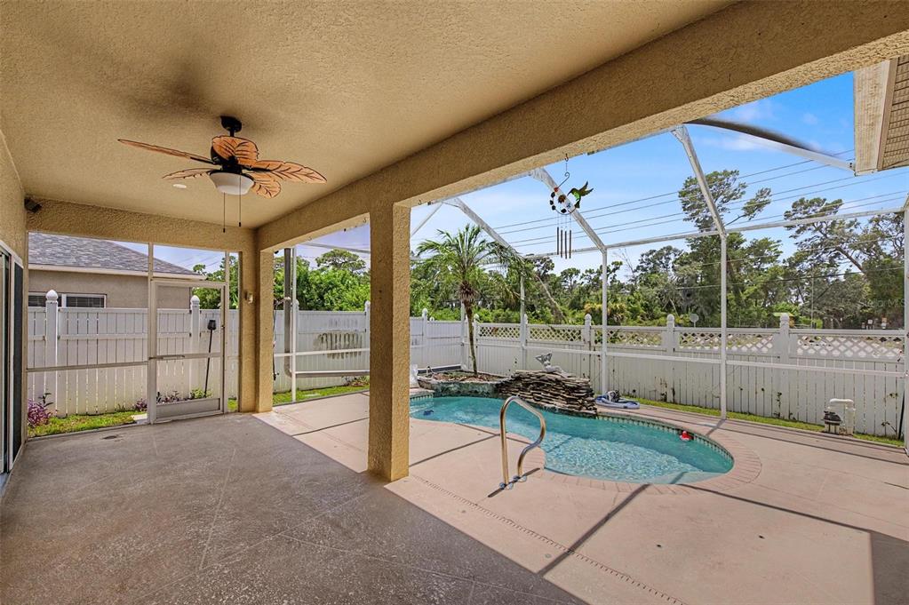 A covered patio with a ceiling fan overlooks a small pool inside a screened enclosure — 2811 RAVENDALE LANE, HOLIDAY, FL