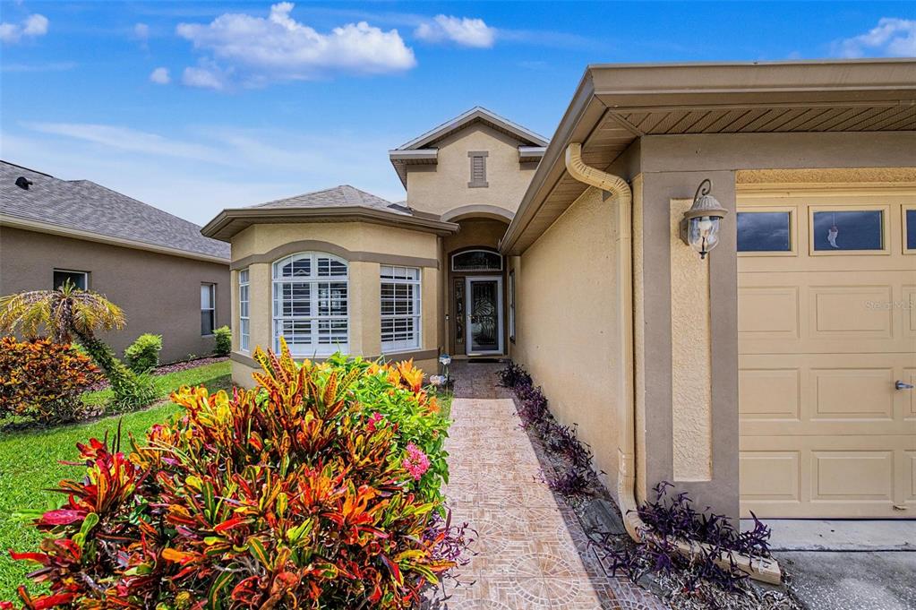 The exterior of a tan stucco house features a tiled walkway leading to the front entrance — 2811 RAVENDALE LANE, HOLIDAY, FL