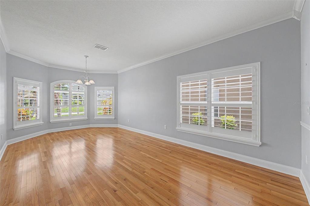 An empty dining room with light gray walls, hardwood floors, and white plantation shutters — 2811 RAVENDALE LANE, HOLIDAY, FL