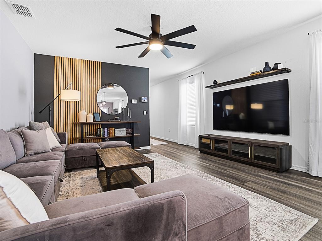 A living room features a grey sectional sofa, wood-slat accent wall, and a large television — 6149 GALLOPING DRIVE, APOPKA, FL