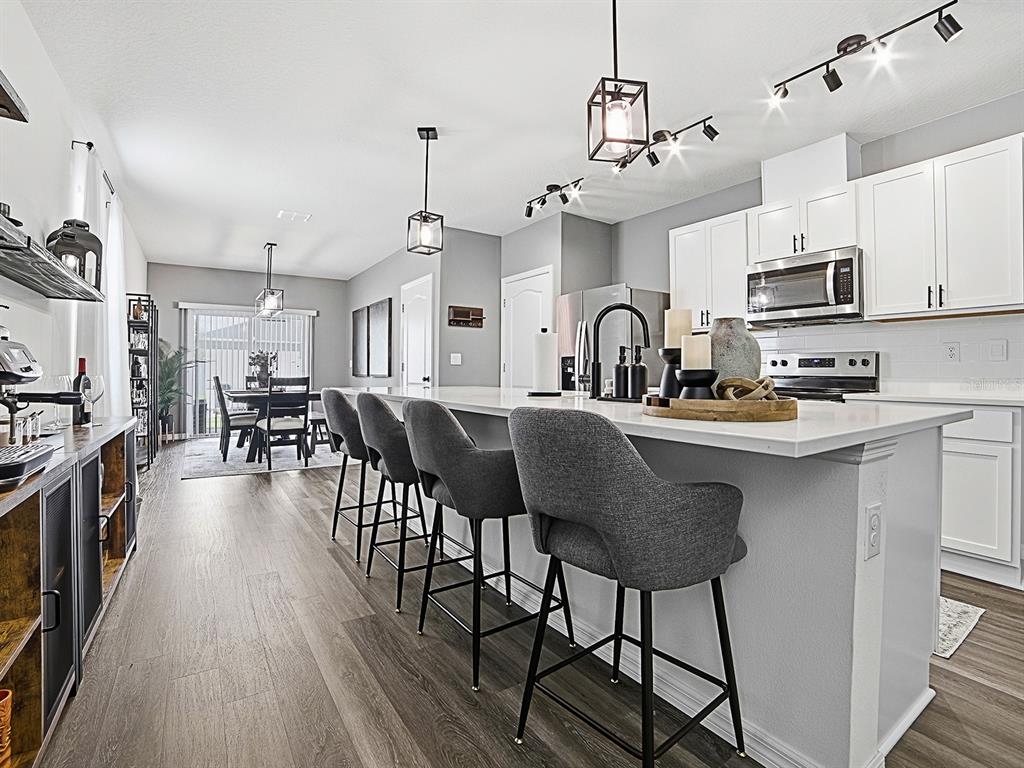 A modern kitchen features a large white island with grey bar stools and pendant lighting — 6149 GALLOPING DRIVE, APOPKA, FL