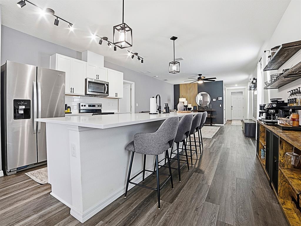 A modern kitchen features a large white island with gray stools and stainless steel appliances — 6149 GALLOPING DRIVE, APOPKA, FL