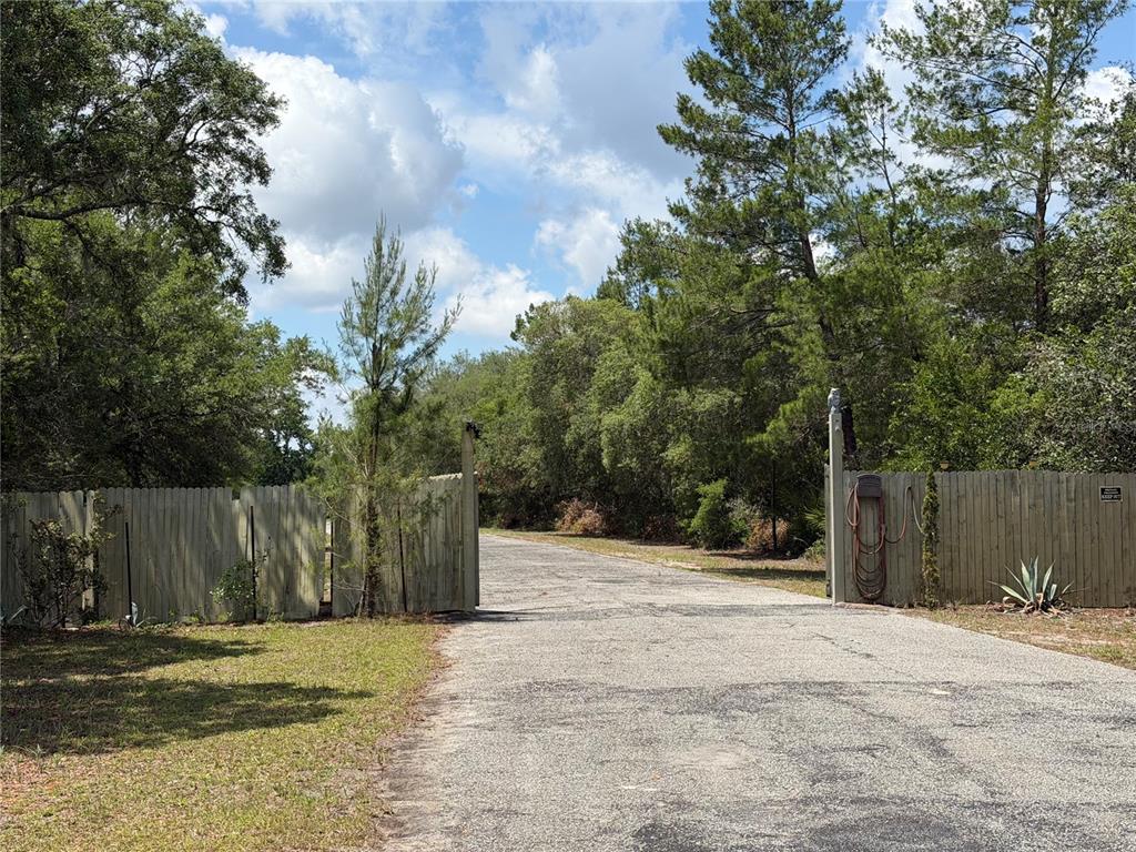 An open wooden gate leads to a paved driveway surrounded by trees and foliage — S SEQUOIA WAY, EUSTIS, FL