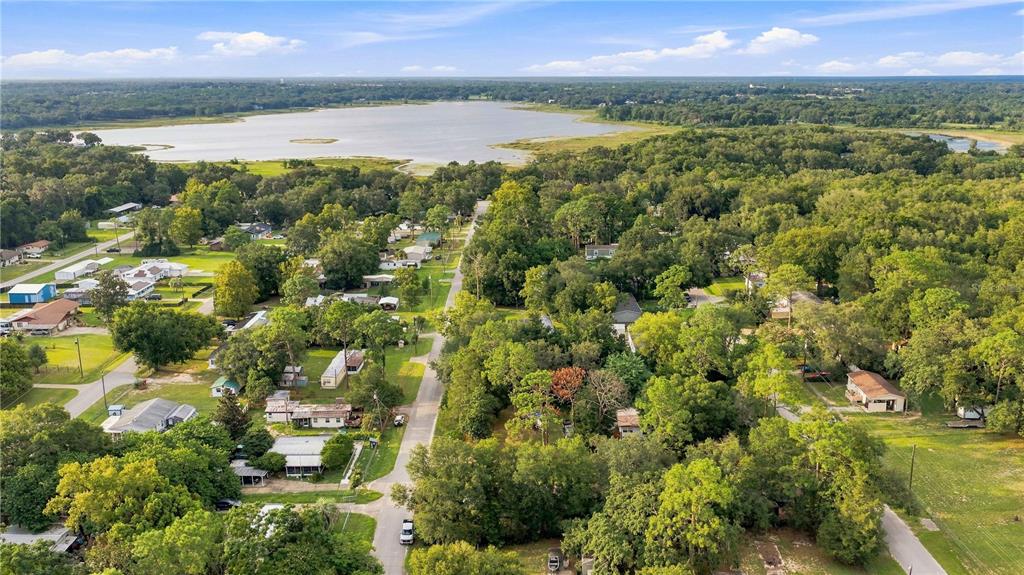 An aerial view shows a residential neighborhood with scattered houses surrounded by trees near a lake — 11945 SE 99TH COURT, BELLEVIEW, FL