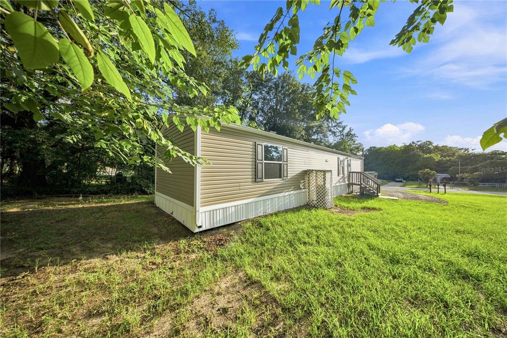 A tan mobile home sits on a grassy lot under a bright blue sky — 11945 SE 99TH COURT, BELLEVIEW, FL