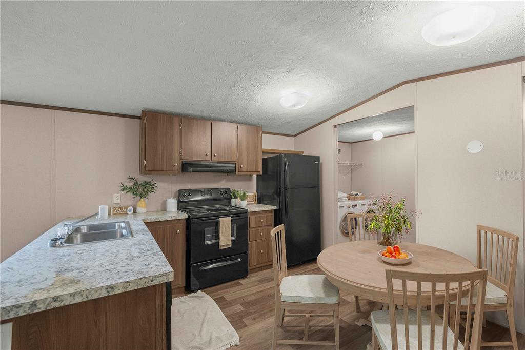 An open-concept kitchen and living area features wood-look flooring, wooden cabinets, and a round table — 11945 SE 99TH COURT, BELLEVIEW, FL