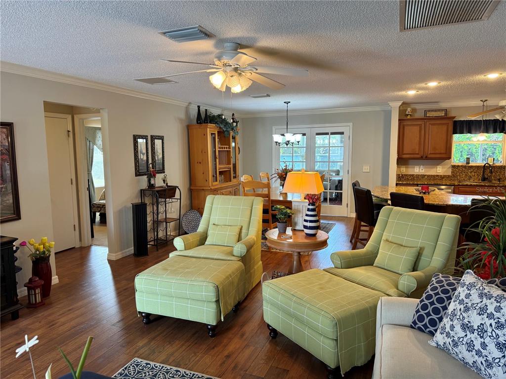 A living room features two green plaid armchairs with ottomans, wood flooring, and an adjacent kitchen — 2417 TATUM TERRACE, THE VILLAGES, FL