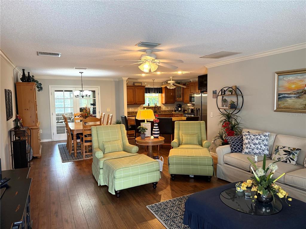An open-concept living and dining area features hardwood floors, light green armchairs, and a kitchen — 2417 TATUM TERRACE, THE VILLAGES, FL