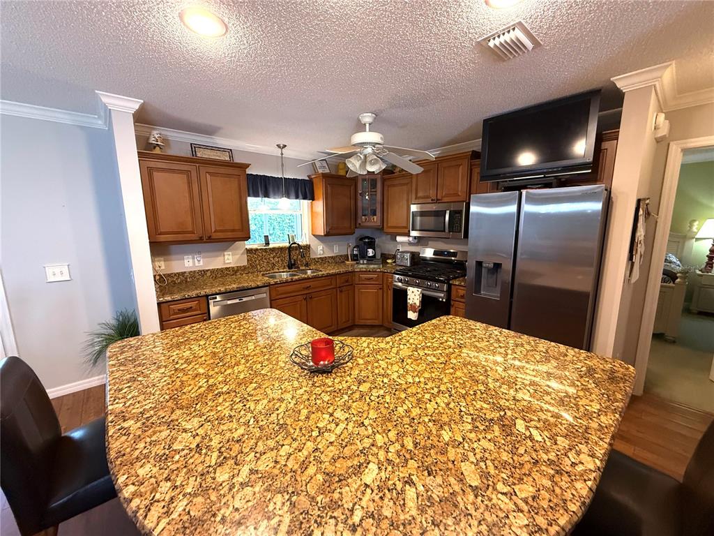A kitchen features granite countertops, wood cabinets, stainless steel appliances, and a central island — 2417 TATUM TERRACE, THE VILLAGES, FL