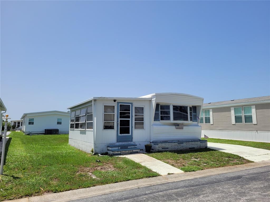 A white mobile home with a screened-in porch and a concrete walkway sits on grass — 3332 SPANISH OAK TERRACE, SARASOTA, FL