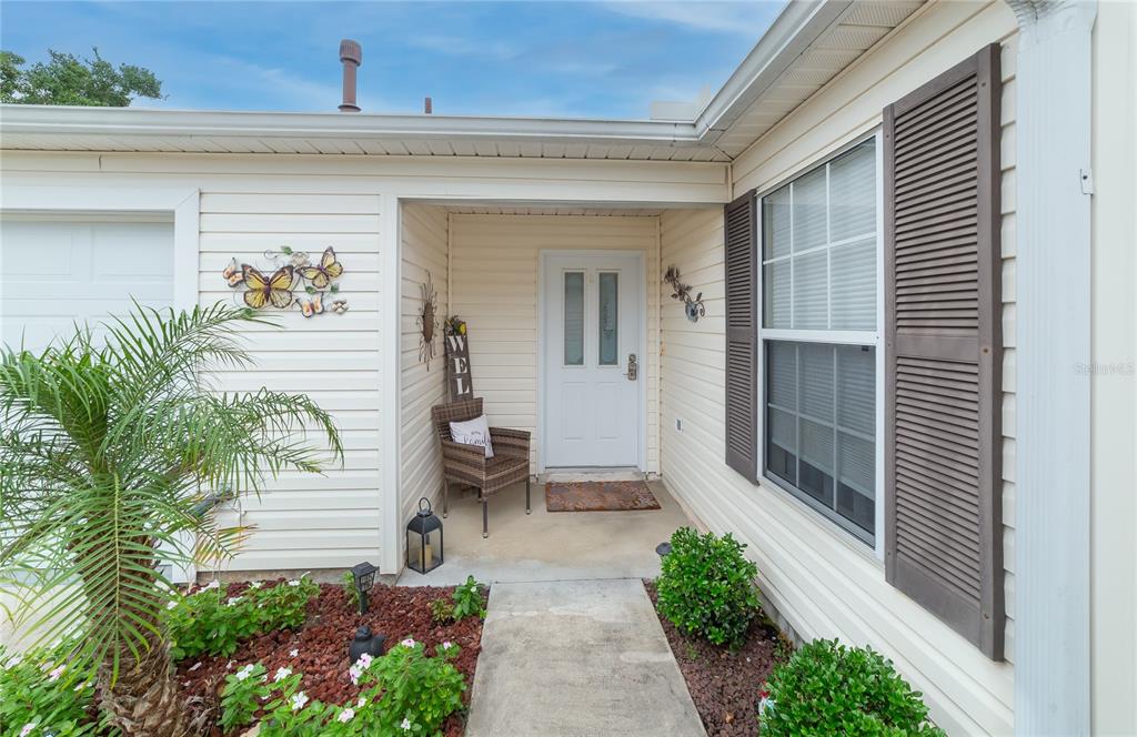 An entryway features a white front door, tiled flooring, and decorative wall signs — 7618 SE 171ST SUN VALLEY PLACE, THE VILLAGES, FL