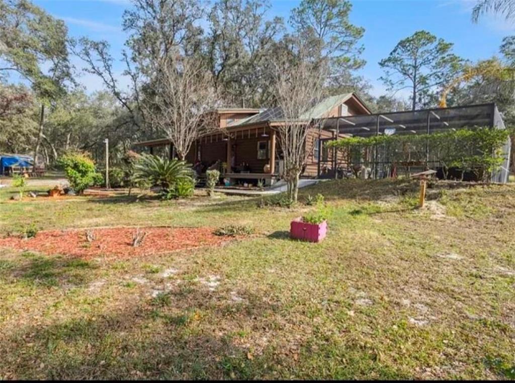 A wooden house with a front porch and a large screened-in patio sits on grass — 1208 DARCY ROAD, LADY LAKE, FL