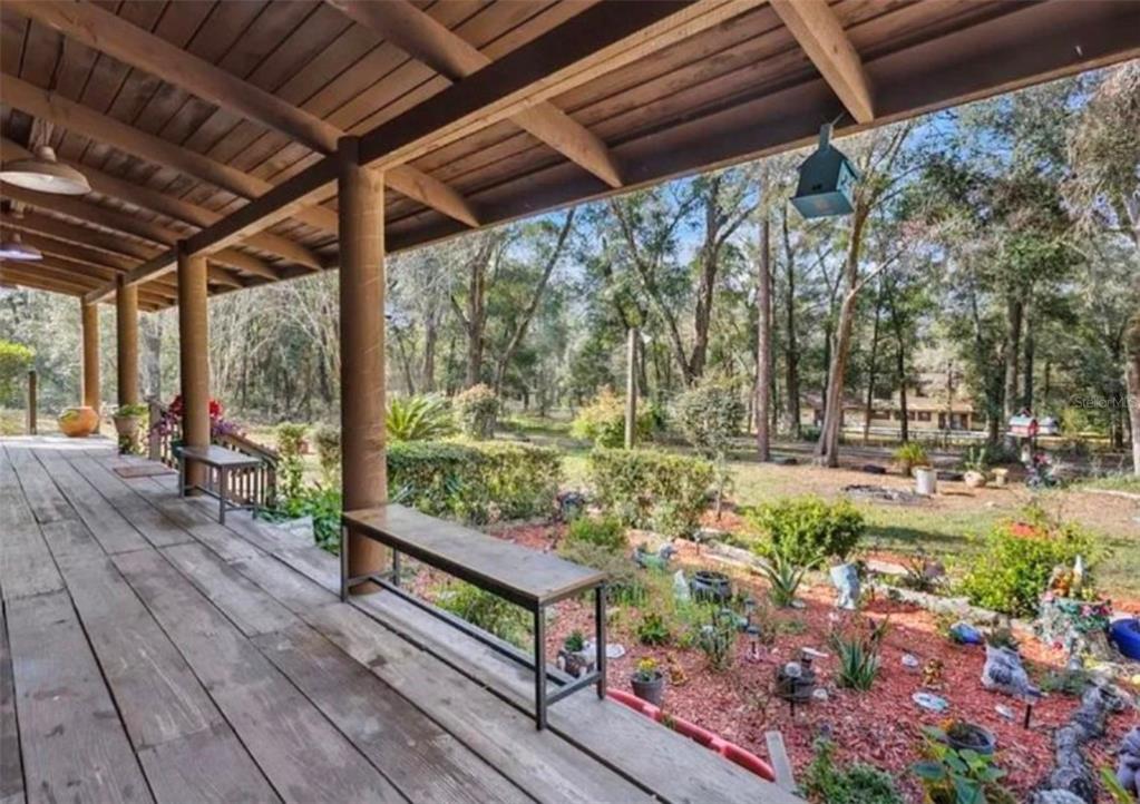 A wooden porch with benches overlooks a landscaped yard with trees and garden decor — 1208 DARCY ROAD, LADY LAKE, FL