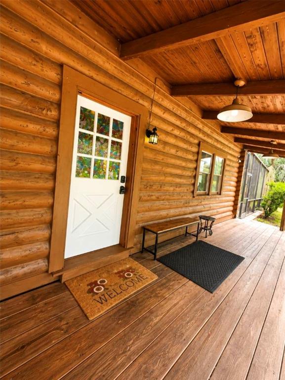 A wooden porch features a white door with stained glass, a bench, and two mats — 1208 DARCY ROAD, LADY LAKE, FL