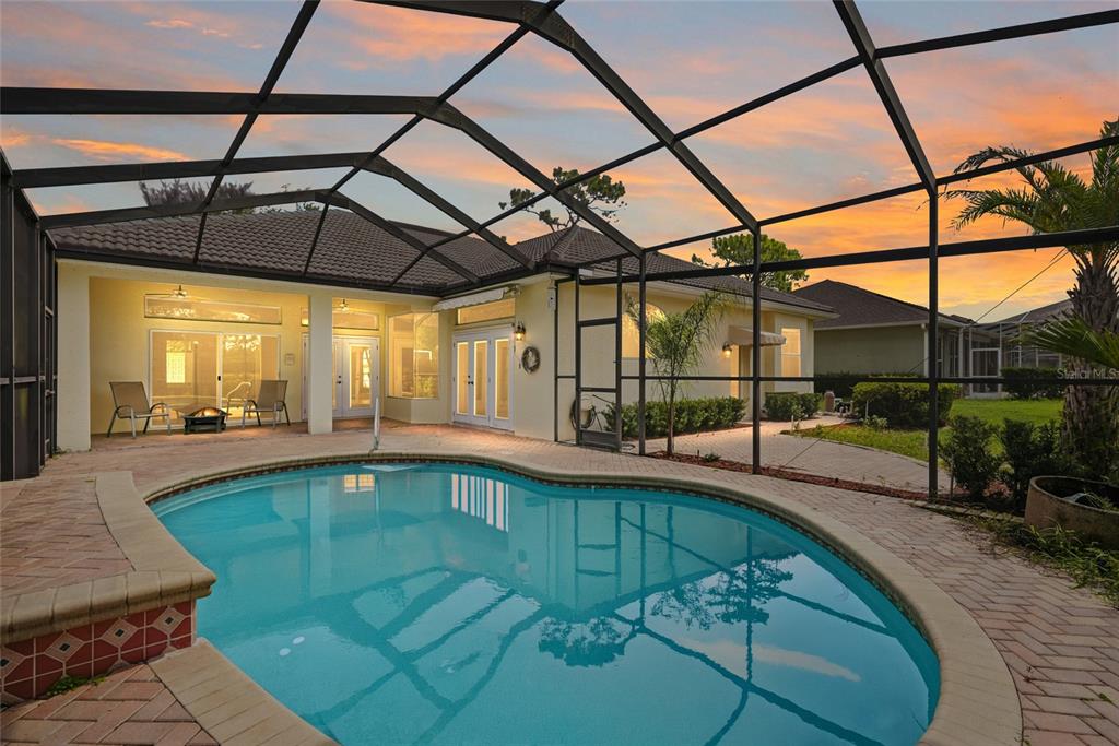 A screened-in patio features a kidney-shaped swimming pool and brick pavers at sunset — 5326 LEGEND HILLS LANE, SPRING HILL, FL