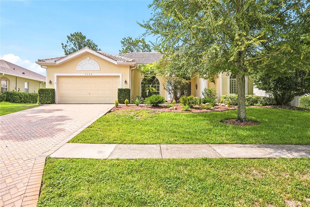 A single-story house with a beige stucco exterior, a tiled roof, and a paved driveway — 5326 LEGEND HILLS LANE, SPRING HILL, FL