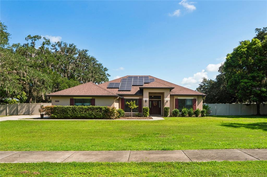 A single-story house with a brown roof, solar panels, and a large front lawn — 27725 CENTURY OAKS COURT, DADE CITY, FL
