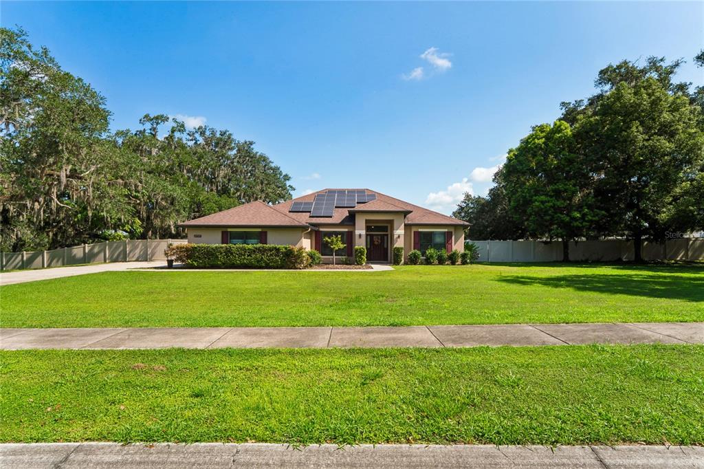 A single-story house with a brown roof, solar panels, and a large front lawn — 27725 CENTURY OAKS COURT, DADE CITY, FL