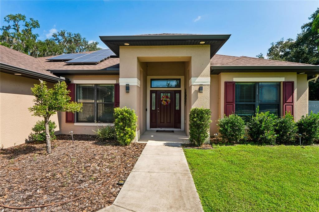 A single-story house with a tan stucco exterior, dark shutters, and a front walkway — 27725 CENTURY OAKS COURT, DADE CITY, FL