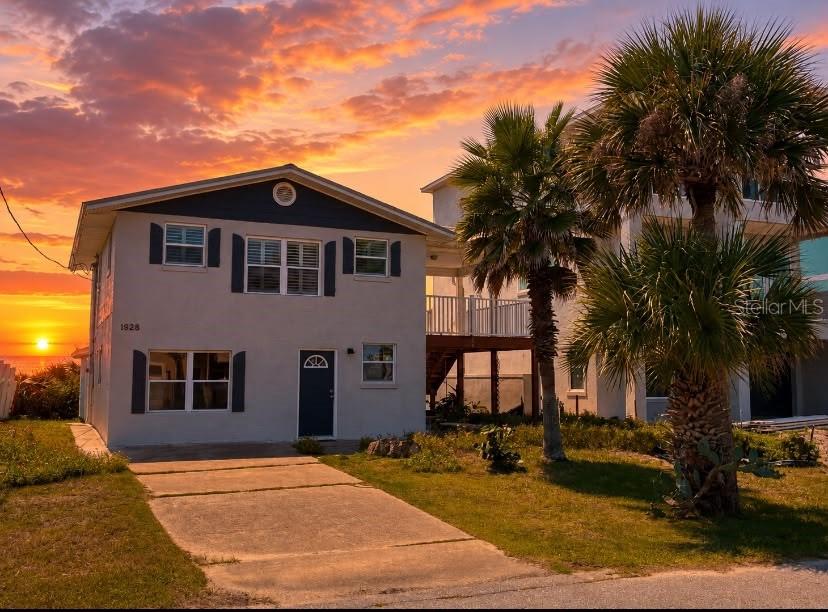 A two-story house with a concrete driveway and palm trees under a vibrant sunset sky — 1828 S CENTRAL AVENUE, FLAGLER BEACH, FL