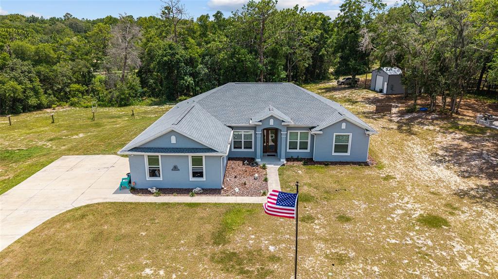 A single-story gray house with a flag pole stands on a grassy lot at dusk — 10254 SE 118TH LANE, BELLEVIEW, FL