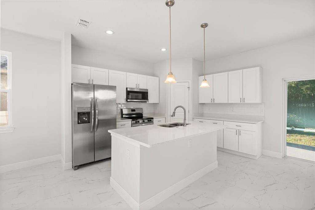 A modern kitchen features white cabinetry, stainless steel appliances, a center island, and tile flooring — 1289 ASH TREE COVE, CASSELBERRY, FL