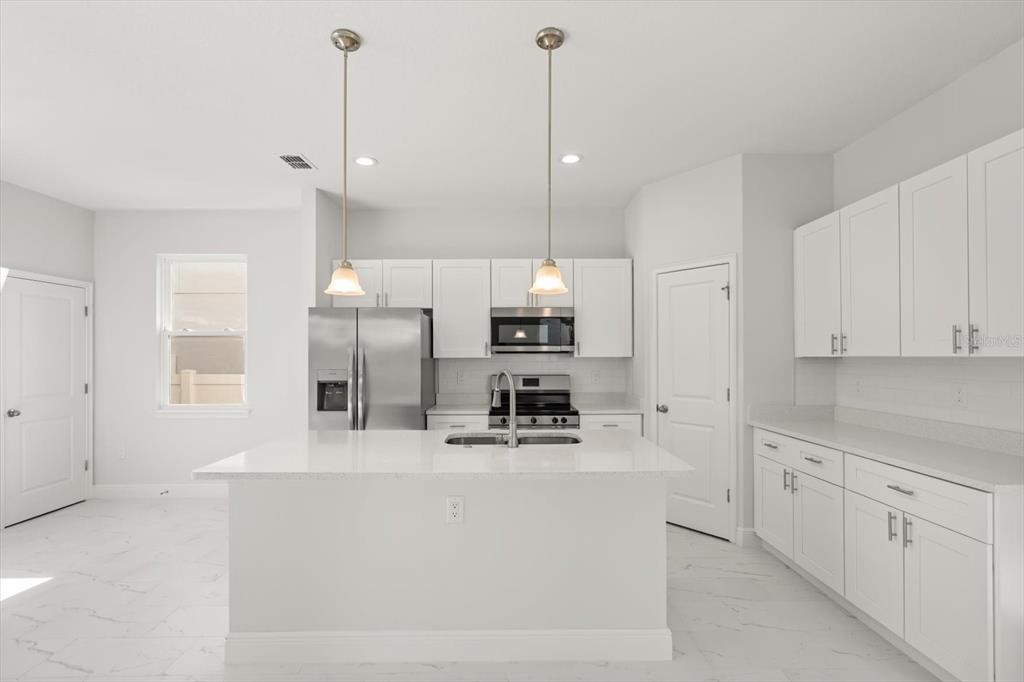 A modern kitchen features white cabinets, stainless steel appliances, a center island, and tile flooring — 1289 ASH TREE COVE, CASSELBERRY, FL