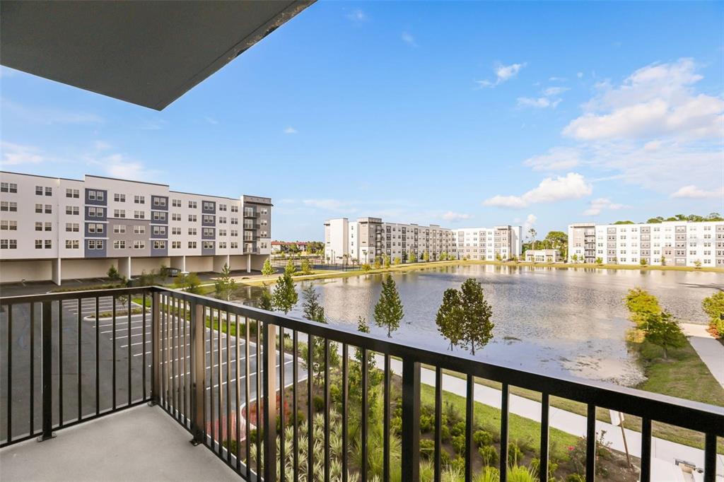 A balcony view overlooks a pond surrounded by modern apartment buildings under a blue sky — 5563 MILLENIA PARK BOULEVARD UNIT 225, ORLANDO, FL