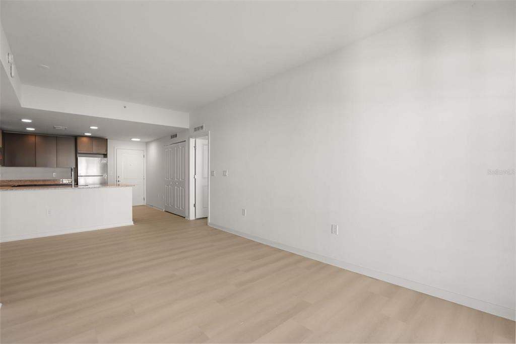 An open-concept living area features light wood-look flooring, white walls, and an adjacent kitchen — 5563 MILLENIA PARK BOULEVARD UNIT 225, ORLANDO, FL