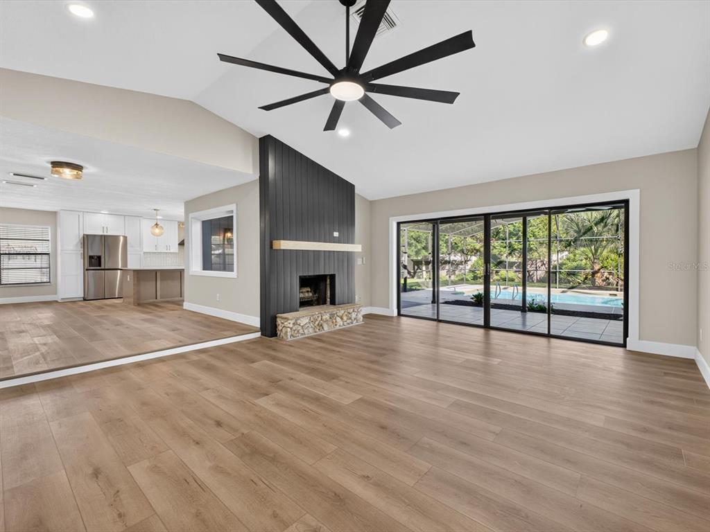 A living room with wood-look flooring, a stone fireplace, and sliding doors overlooking a pool — 2183 BENT OAK DRIVE, APOPKA, FL