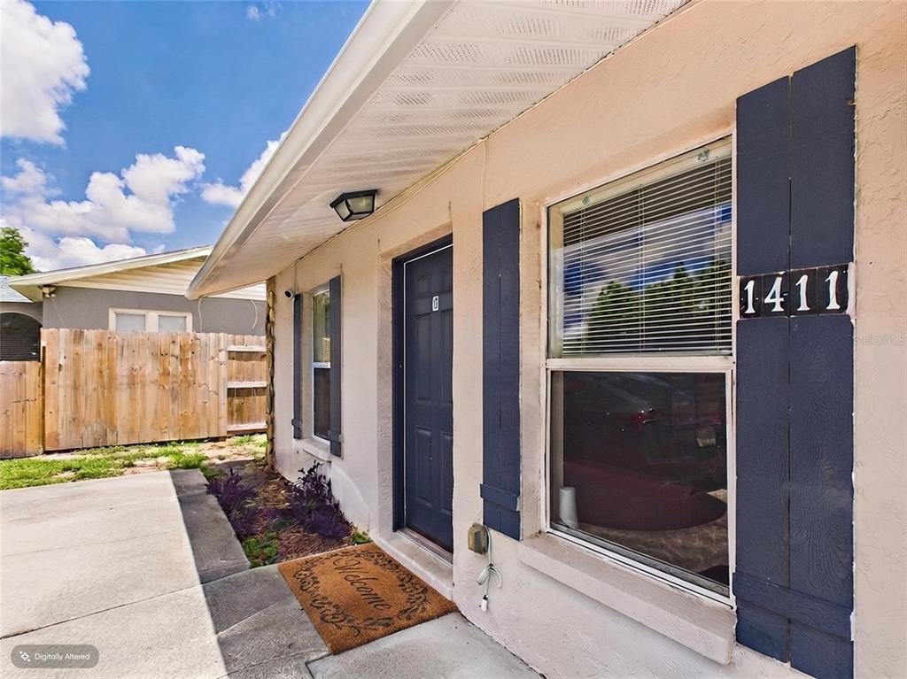 A beige exterior wall features a dark blue door, window shutters, and a house number — 1411 E 109TH AVENUE UNIT B, TAMPA, FL