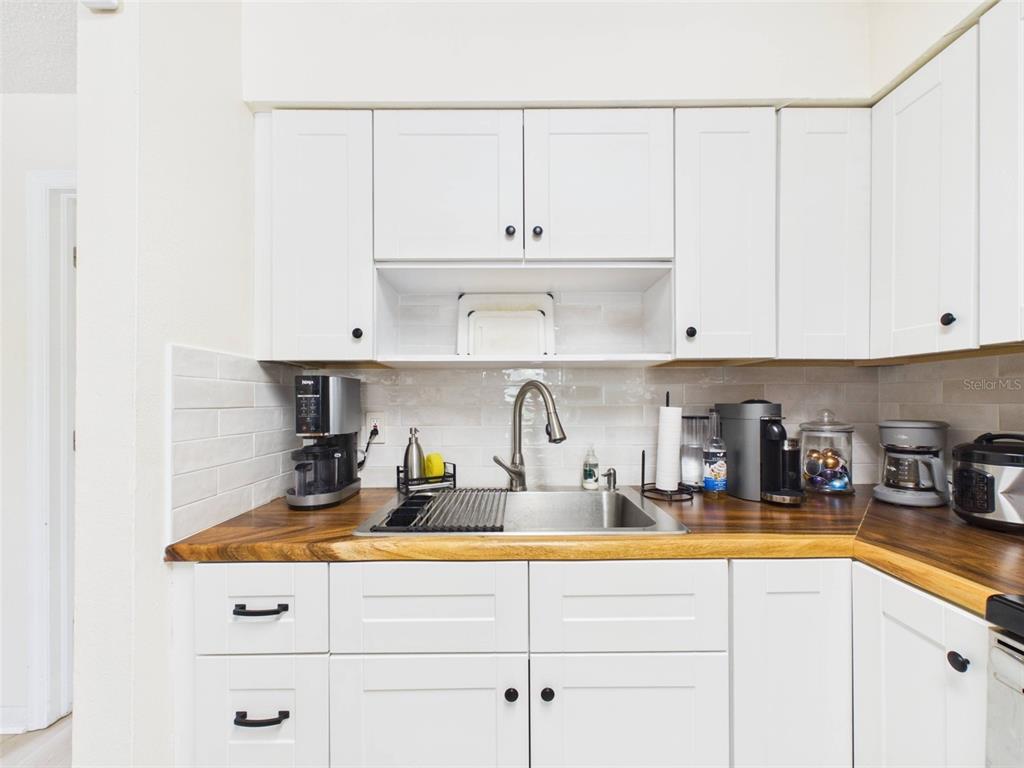 A kitchen features white cabinets, a wood countertop, and a stainless steel sink — 1411 E 109TH AVENUE UNIT B, TAMPA, FL