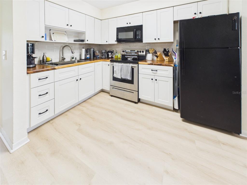A kitchen features white cabinets, wood countertops, stainless steel appliances, and a black refrigerator — 1411 E 109TH AVENUE UNIT B, TAMPA, FL
