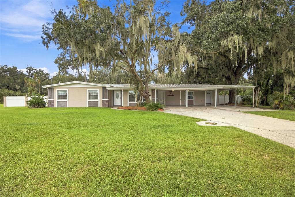 A single-story house with a carport and large oak trees in a grassy yard — 5106 THONOTOSASSA ROAD, PLANT CITY, FL