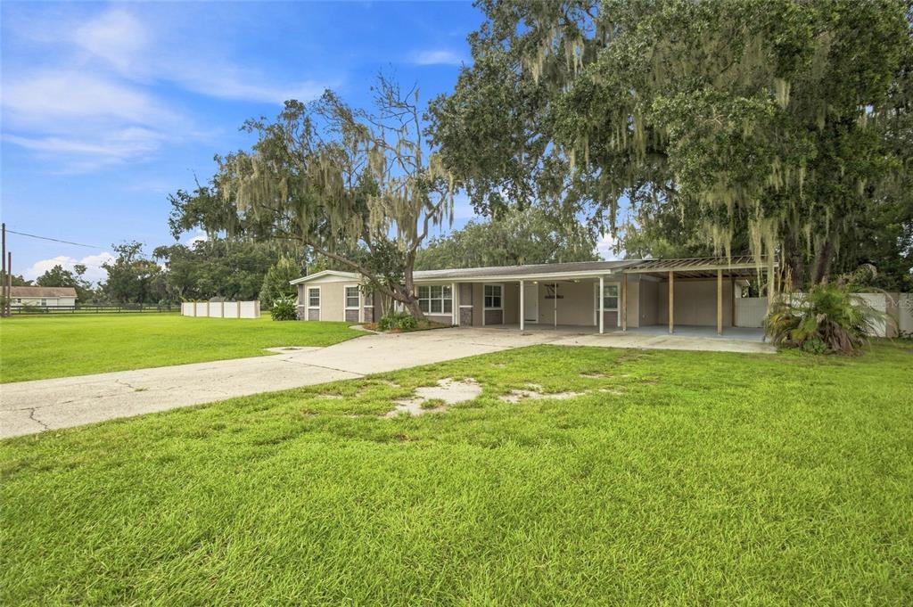 A single-story house with a concrete driveway, a carport, and large trees in the yard — 5106 THONOTOSASSA ROAD, PLANT CITY, FL