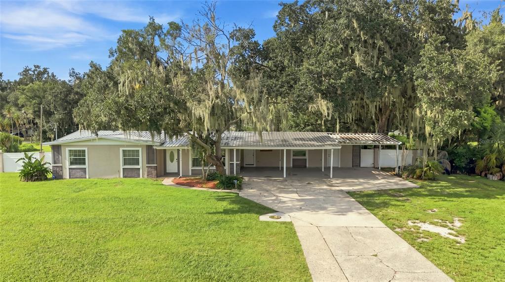 A single-story house with a metal roof, a carport, and large oak trees in front — 5106 THONOTOSASSA ROAD, PLANT CITY, FL