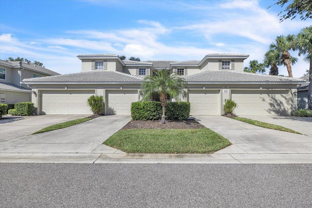 A two-story duplex with four garage doors, a central palm tree, and light-colored stucco siding — 3303 GRAND VISTA COURT UNIT 101, PORT CHARLOTTE, FL