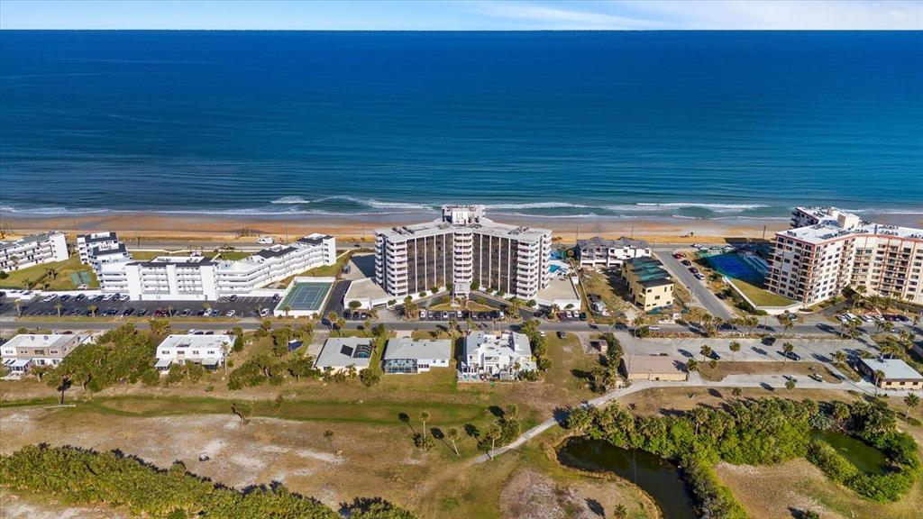 An aerial view shows a multi-story beachfront hotel surrounded by parking lots and coastal vegetation — 3580 S OCEAN SHORE BOULEVARD UNIT 101, FLAGLER BEACH, FL