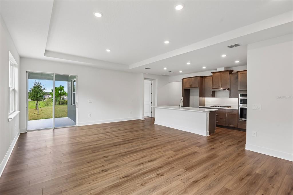An open-concept kitchen and living area features dark wood cabinets, a white island, and flooring — 786 EMERALD GROVE DRIVE, APOPKA, FL