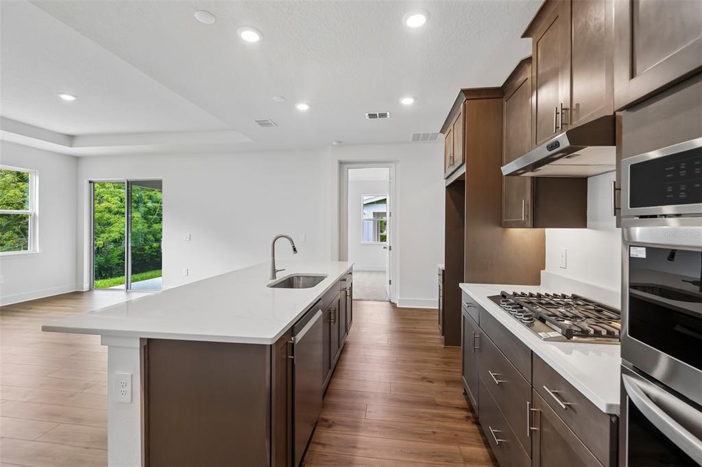 A modern kitchen features dark wood cabinets, white countertops, a center island, and wood-look flooring — 786 EMERALD GROVE DRIVE, APOPKA, FL