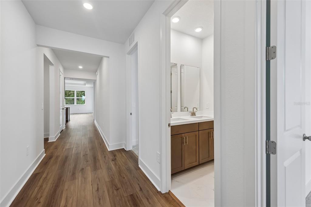 A hallway with wood-look flooring leads to a bathroom with a double-sink vanity — 786 EMERALD GROVE DRIVE, APOPKA, FL