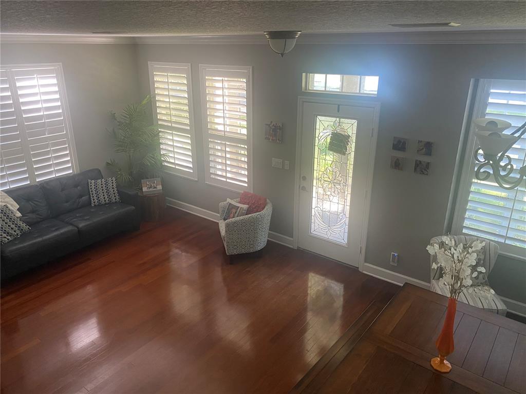 A living room with hardwood floors, a dark leather sofa, and a glass-paneled front door — 108 W LAKE VICTORIA CIRCLE, DELAND, FL