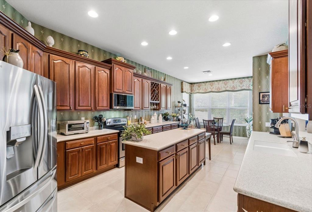 A kitchen with wood cabinets, a central island, and a dining area by the window — 13800 CREST LAKE DRIVE, HUDSON, FL