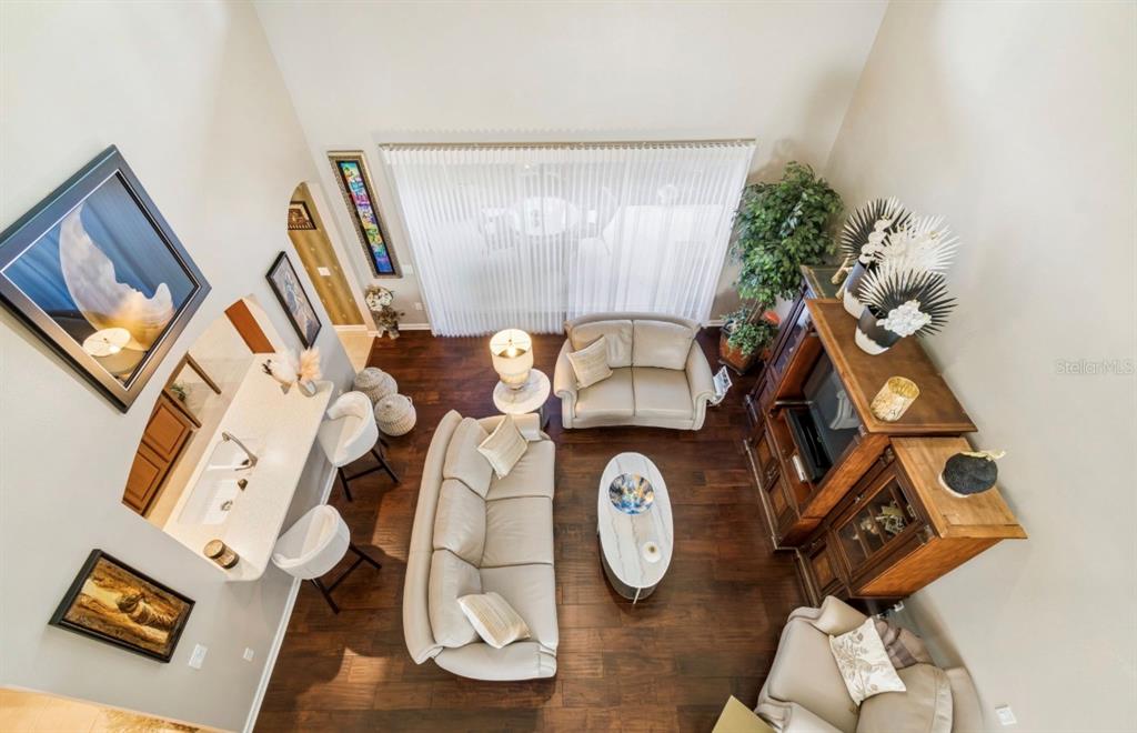 High-angle view of a living room with hardwood floors, white sofas, and a breakfast bar — 13800 CREST LAKE DRIVE, HUDSON, FL