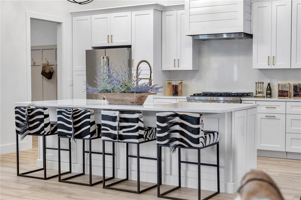 A modern white kitchen features a large island with zebra-print bar stools and stainless appliances — 3750 SE 139TH TERRACE, MORRISTON, FL
